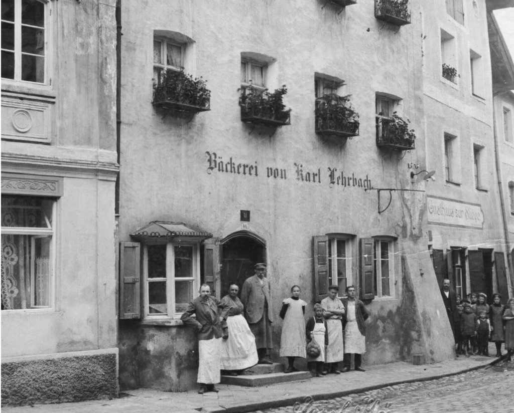 schwarz-weiß Originalaufnahme des ersten Standorts in der Hauptstraße 37 in Trostberg, aufgenommen im Jahr 1905. Davor steht die Familie Lehrbach.