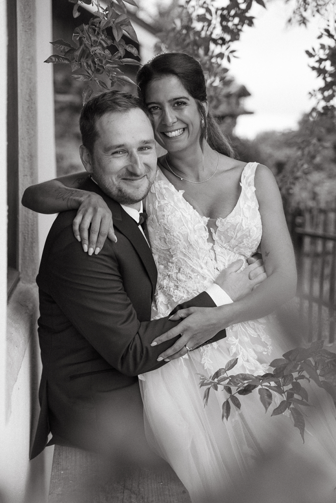 Carina und Frank an ihrem Hochzeitstag. Sie sitzt auf seinem Schoß und leide strahlen in die Kamera.