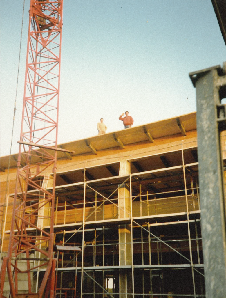 Foto von der Baustelle 1988. Zwei Männer stehen auf dem Dach des neuen Gebäudes. Daneben ein Kran.