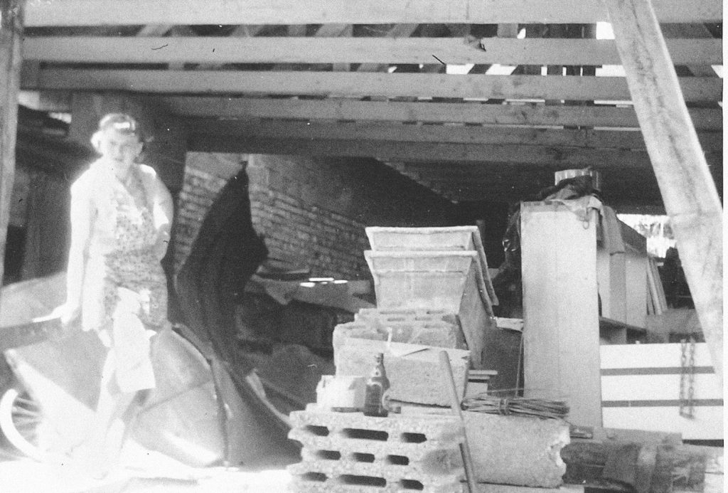 Bild der Baustelle des Umbaus 1961-1964. Eine Frau neben Ziegelsteinen, Tonnen und weiteren Materialien